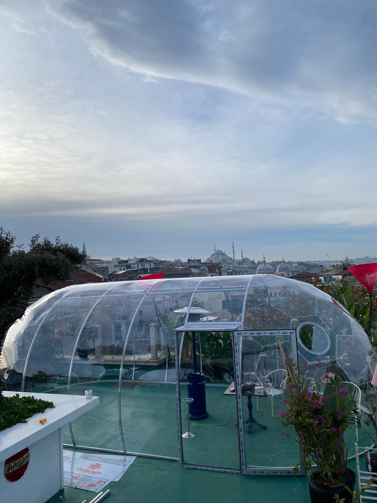 Transparenter Kuppelpavillon mit geöffneter Tür auf einer begrünten Dachterrasse