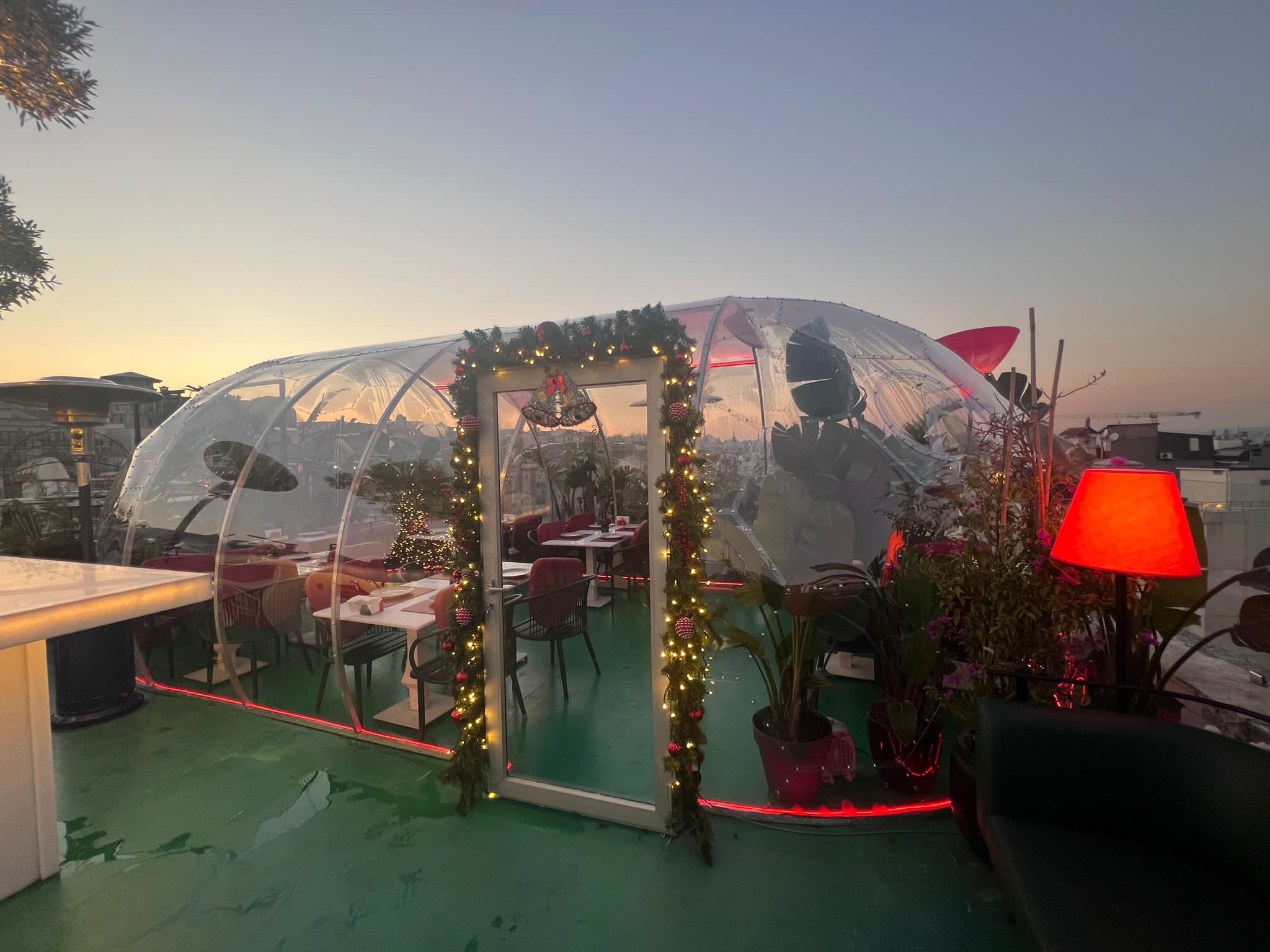 Länglicher transparenter Kuppelpavillon mit gedeckten Tischen und Lichterdekoration bei Sonnenuntergang
